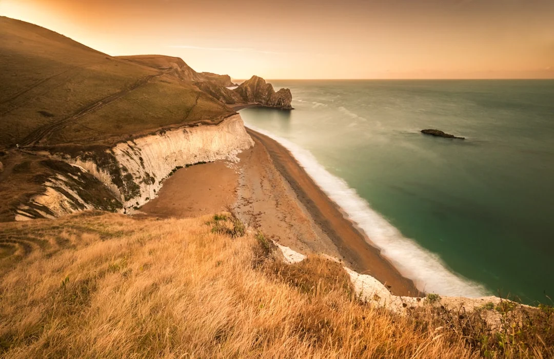 Golden sunrise over white cliffs and a pebble beach at Durdle Door, Dorset, with calm turquoise sea