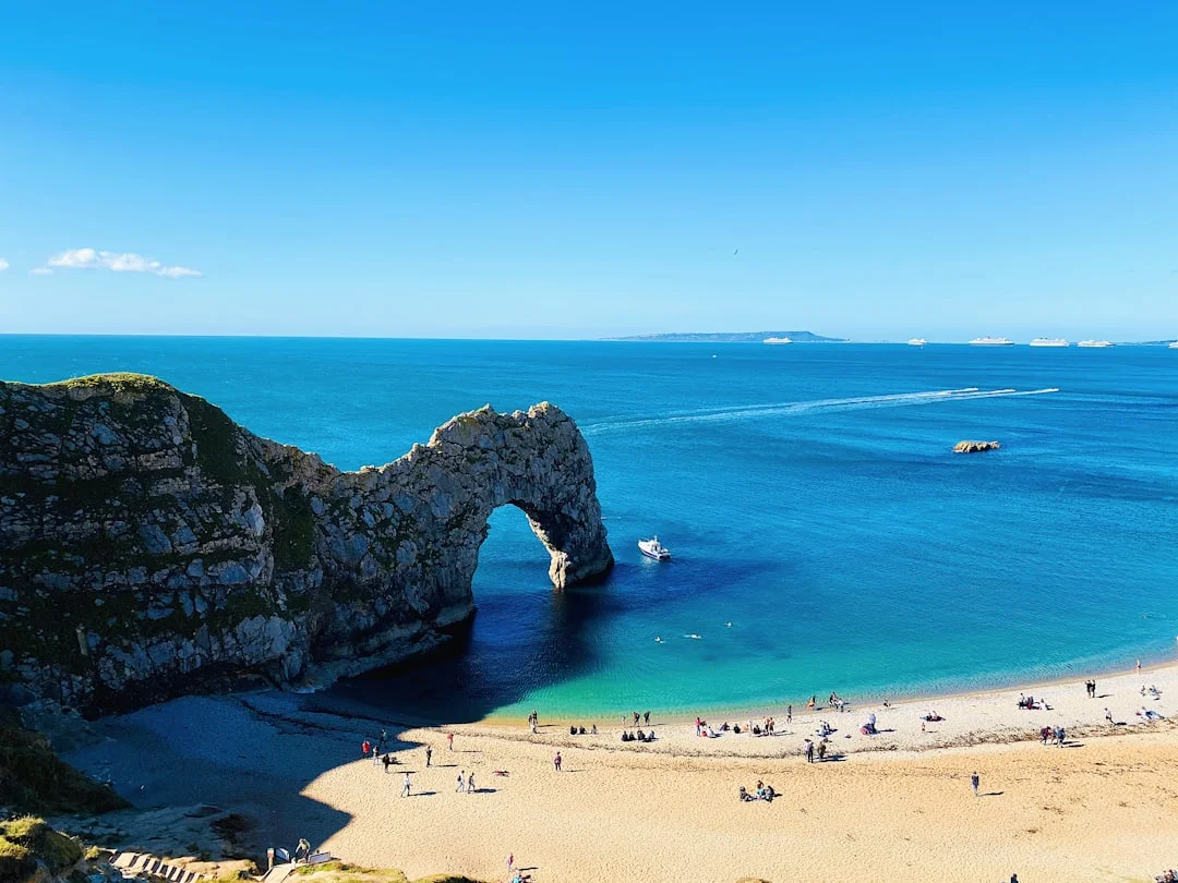 People on a sandy beach next to a natural limestone arch in clear blue water on the Dorset coast