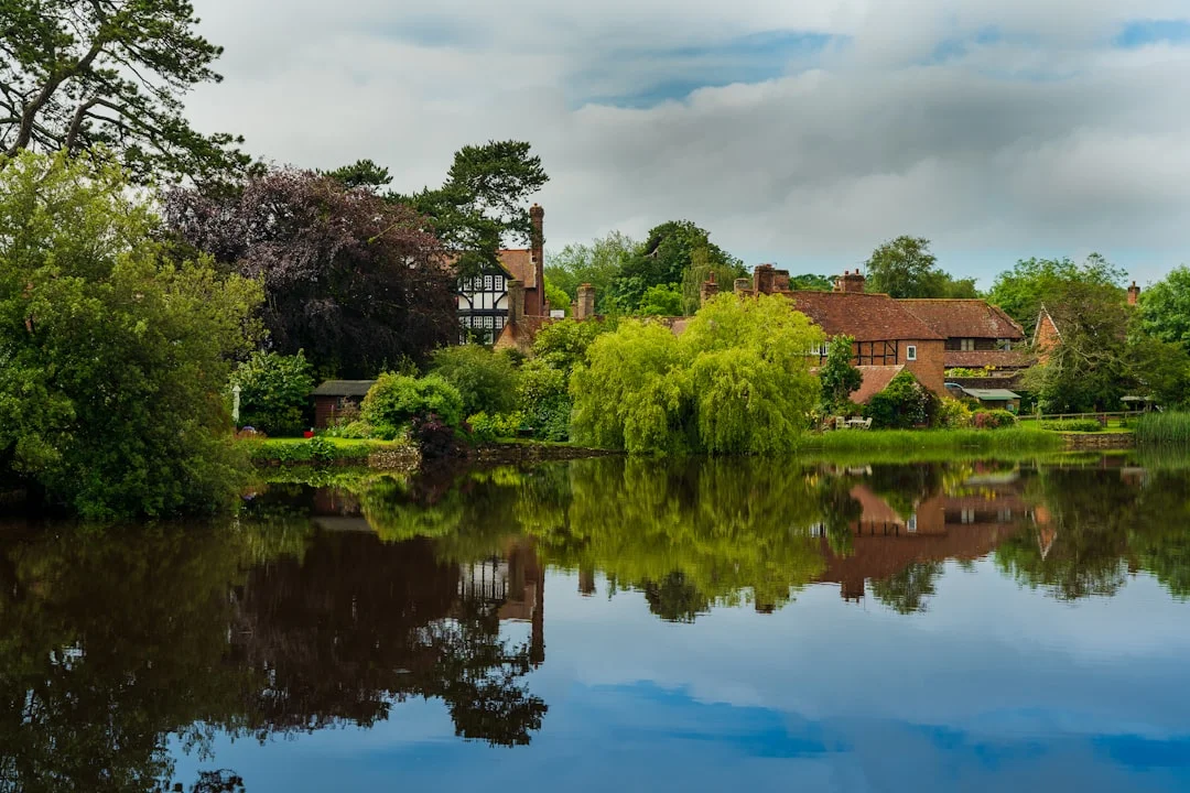 Traditional houses and lush green trees reflected in the calm waters of a lake in Beaulieu, Hampshire