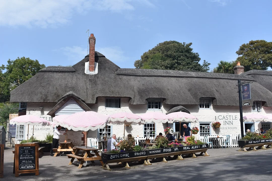 A traditional thatched-roof pub with pink umbrellas and outdoor picnic tables at The Castle Inn