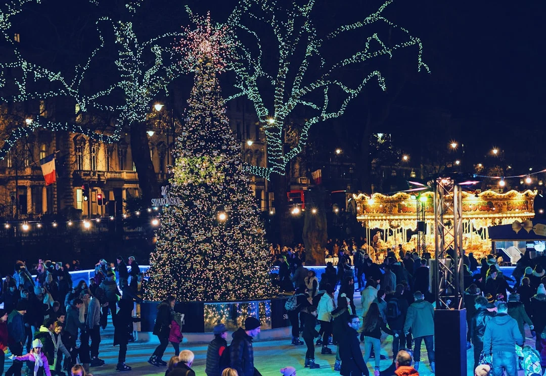 People ice skating around a large, illuminated Christmas tree at a festive outdoor market at night