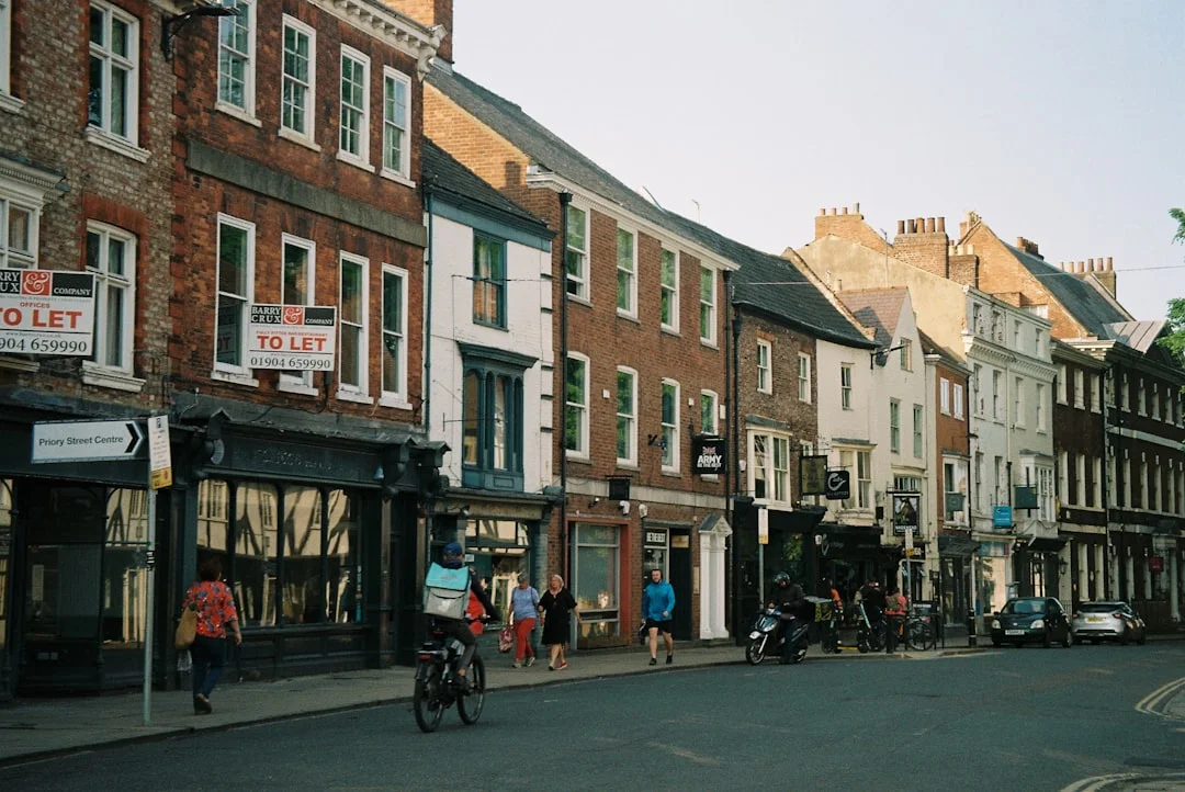 People walking and cycling past traditional brick buildings and shops on Greek Street in Leeds