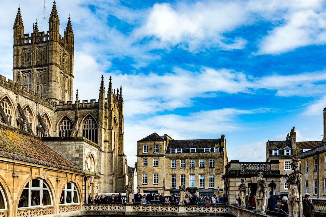 Historic Bath Abbey and Roman Baths with stone statues under a blue sky in Somerset, England