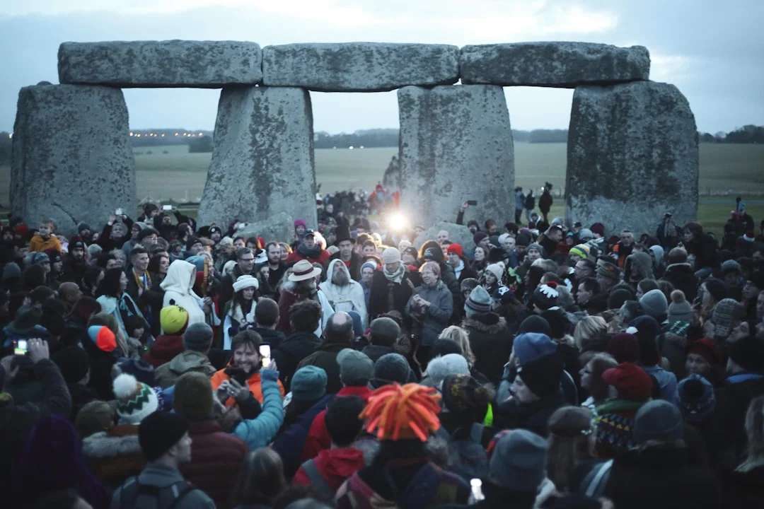 A large crowd gathers at Stonehenge during the winter solstice at dawn, wearing warm winter clothing