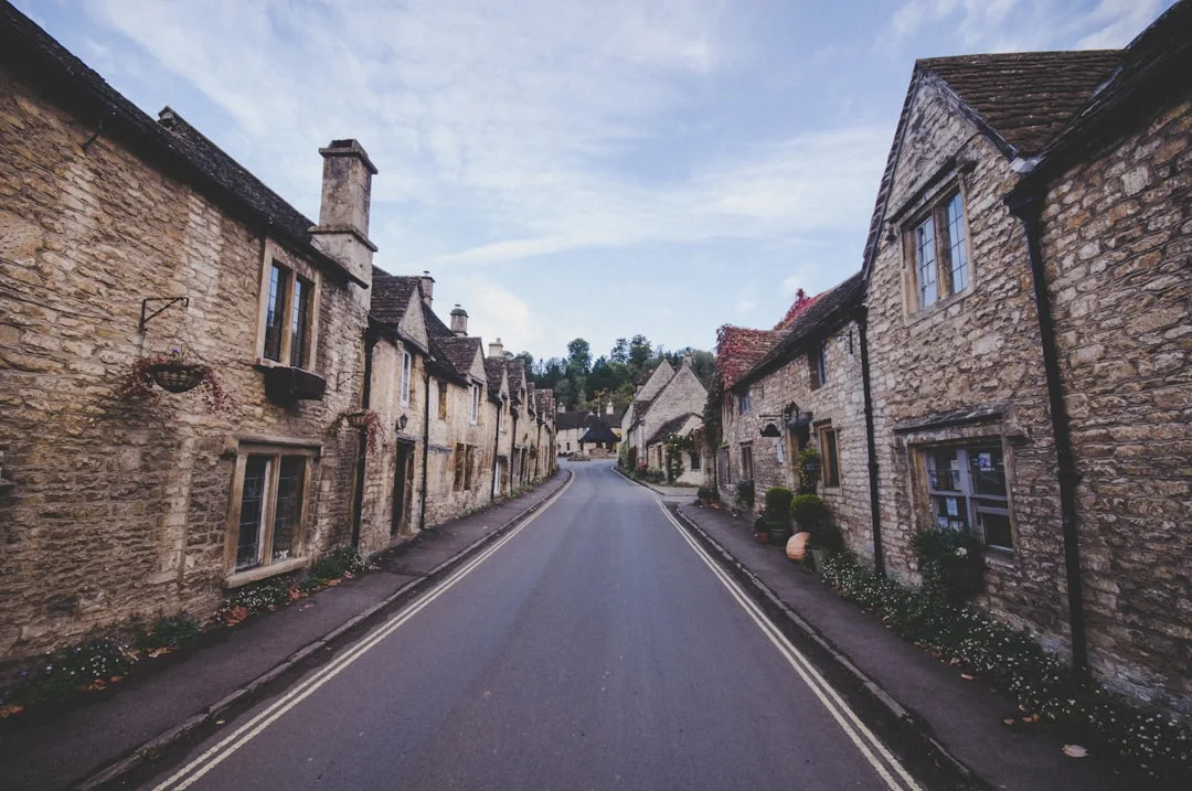 A narrow asphalt road lined with traditional stone cottages under a blue sky in a Wiltshire village