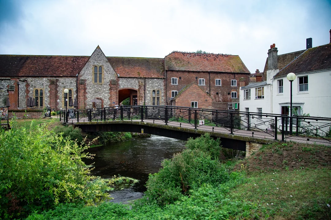 A small footbridge crosses a river in front of historic stone and brick buildings in Salisbury