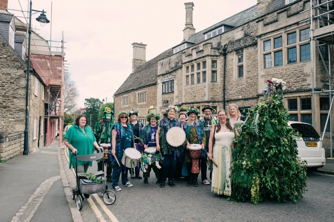 A group in green folk costumes with drums and a large leafy figure on a historic Wiltshire street