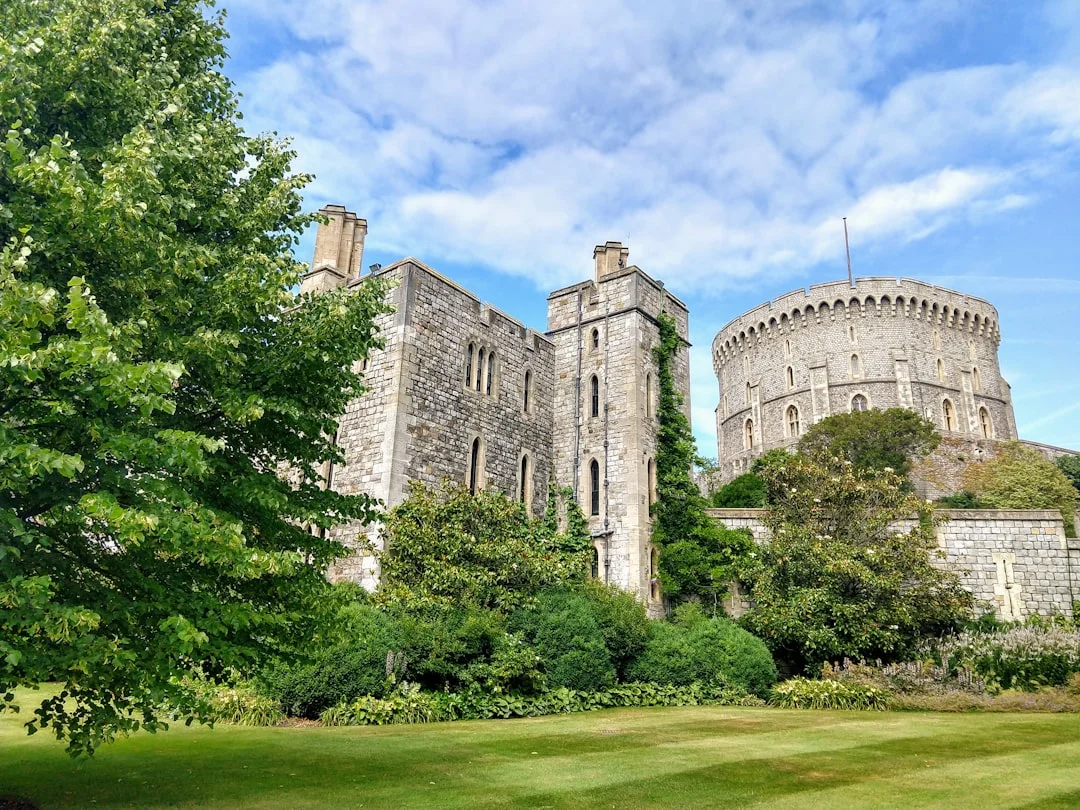 Stone walls and the Round Tower of Windsor Castle viewed from a lush green garden under a blue sky