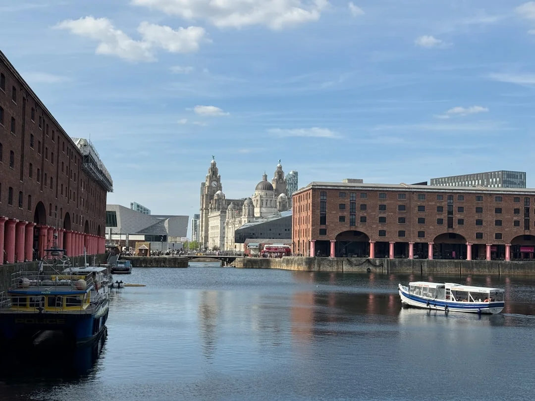 Liverpool Albert Dock with historic brick warehouses, boats on the water, and the iconic Liver Building under a blue sky