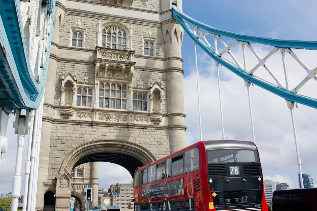Red double-decker bus crossing Tower Bridge in London with blue suspension cables visible