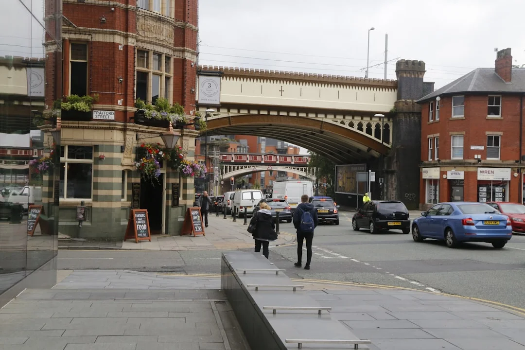 Manchester Northern Quarter street with a red brick building, railway bridge, and passing cars