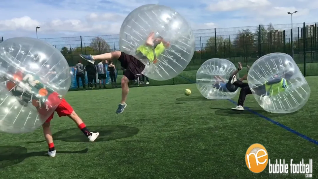 A group of women laughing while playing bubble football outdoors on a sunny day.
