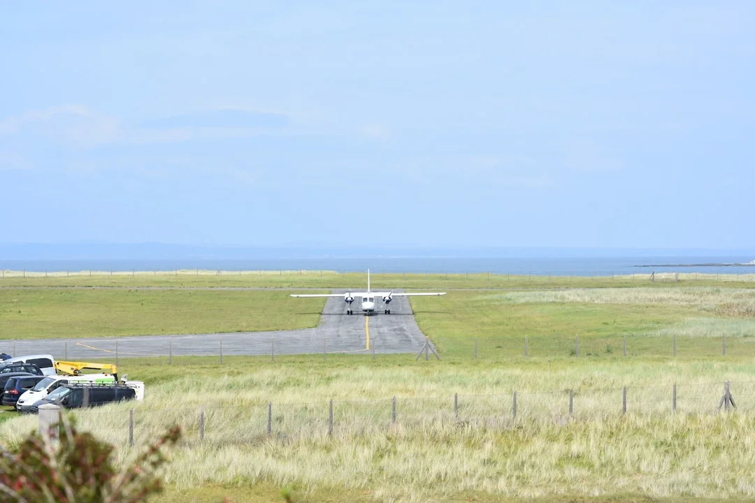 A small airplane sits on a runway at Cornwall Airport Newquay with the ocean visible in the distance