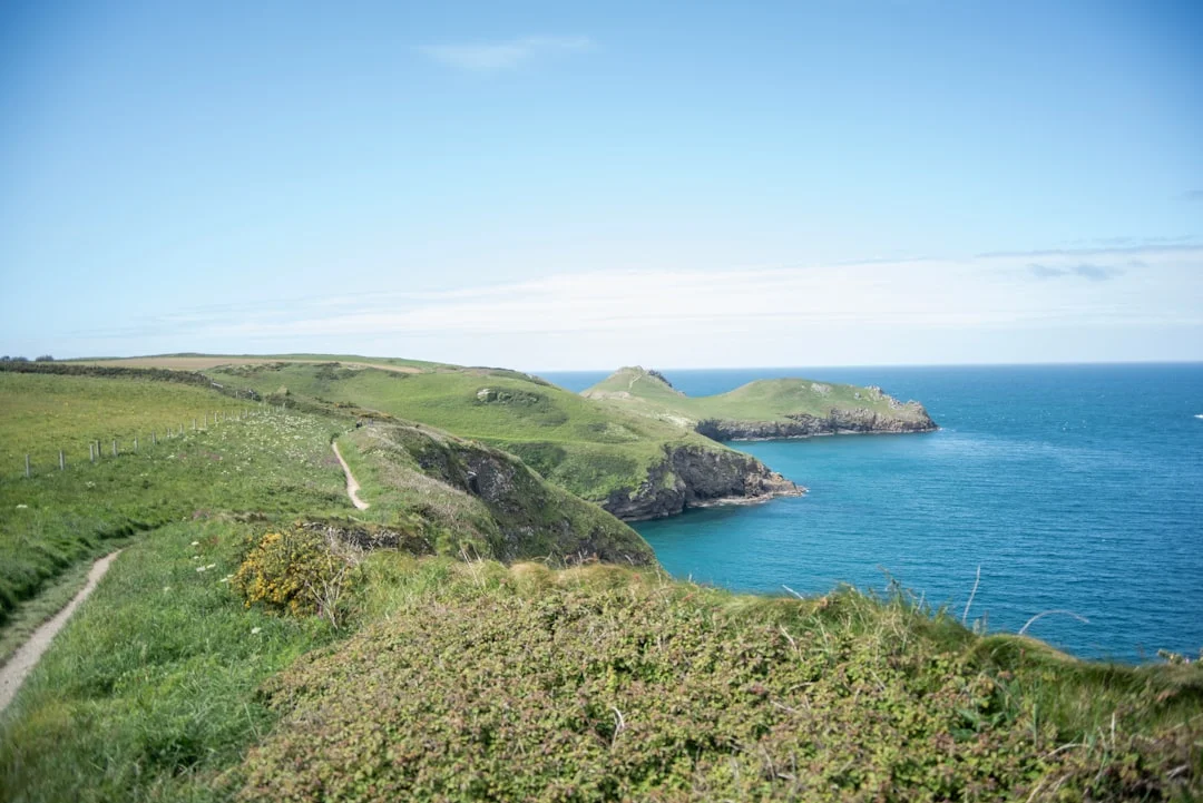 Green coastal cliffs and a walking path overlooking a blue ocean with rocky islands in the distance