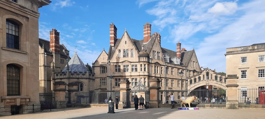 Historic stone buildings in Oxford with the Bridge of Sighs and a golden ox statue under a blue sky