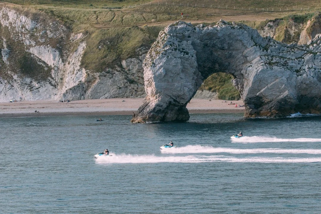 A group on jet skis speeding along the Jurassic Coast near Weymouth, with dramatic cliffs in the background.