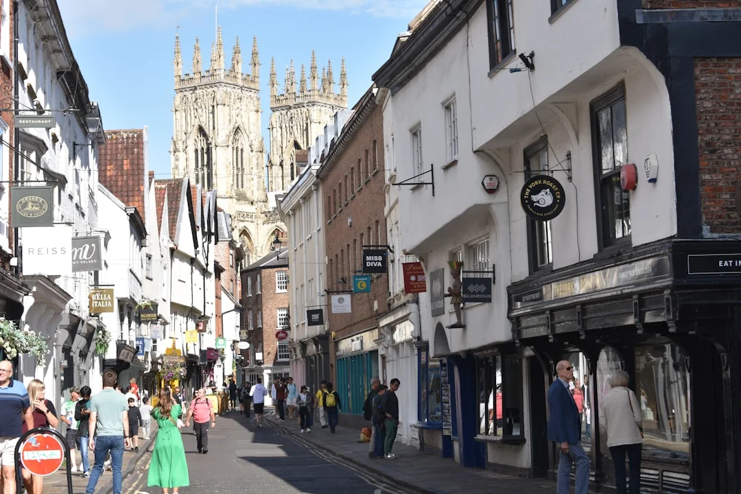 Pedestrians walk along a narrow street in York with the towers of York Minster in the distance