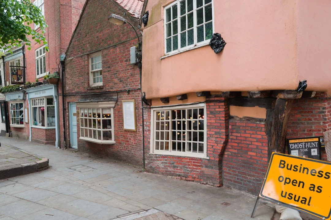 Old brick and timber buildings on a York street with a yellow sign reading Business open as usual